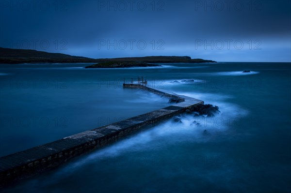 Sea surf on concrete jetty at blue hour