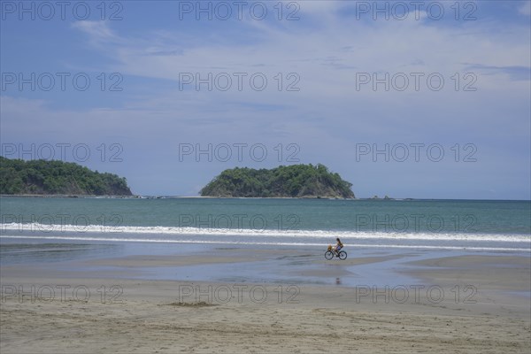 Woman riding a bicycle on the beach of Samara in the background Chora Island