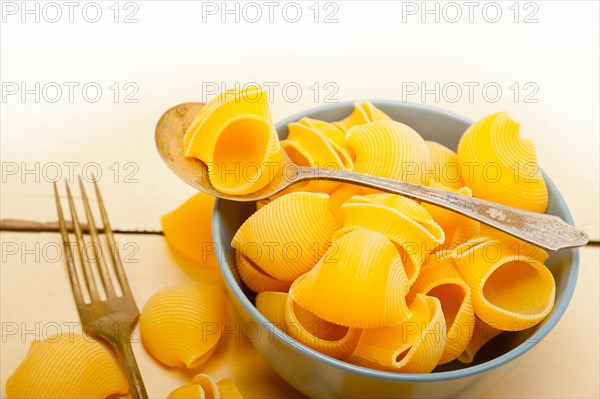 Raw Italian snail lumaconi pasta on a blue bowl over rustic table macro