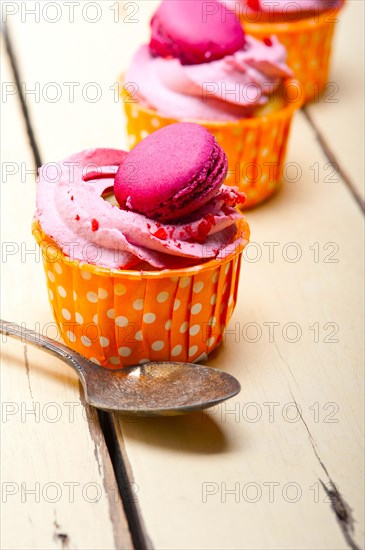 Fresh pink berry cream cupcake with macaroon on top over rustic wood table