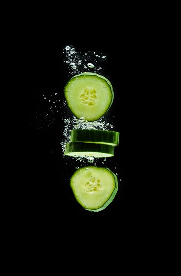 Sliced bio cucumber splashing water isolated on black background