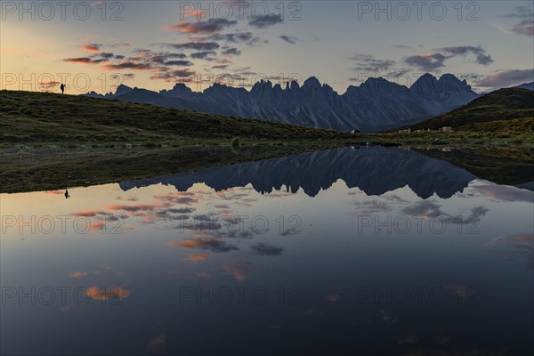 Salfainsee with reflection of the Kalkkoegel and mountaineers on mountain meadow at sunrise