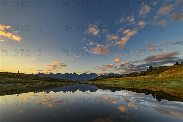 Salfainsee with reflection of the Kalkkoegel and mountaineers on mountain meadow at sunrise