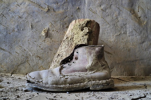 Ailing leather work boot stands on a wall