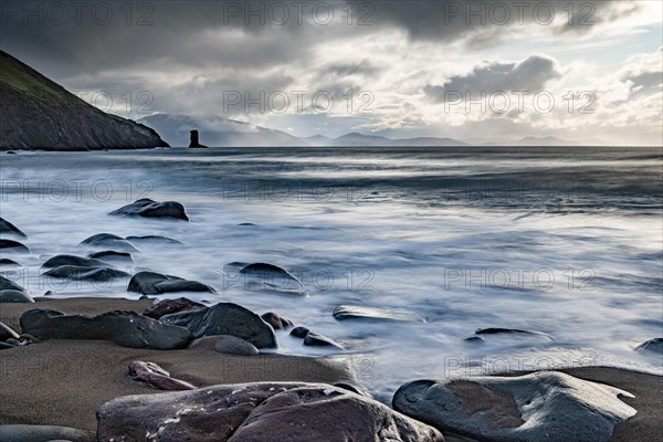 Sandy beach beach with stones on North Atlantic with rocky outcrop and cloudy sky