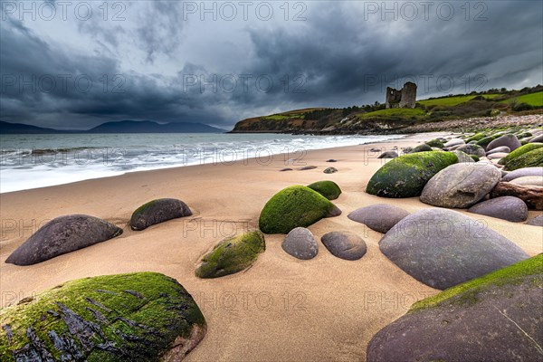 Sandy beach beach with moss-covered stones and Minard Castle in the background