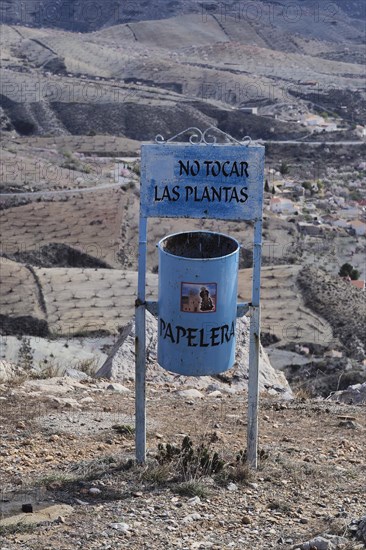 Blue litter bin in front of almond plantation at Virgin de Saliente monastery