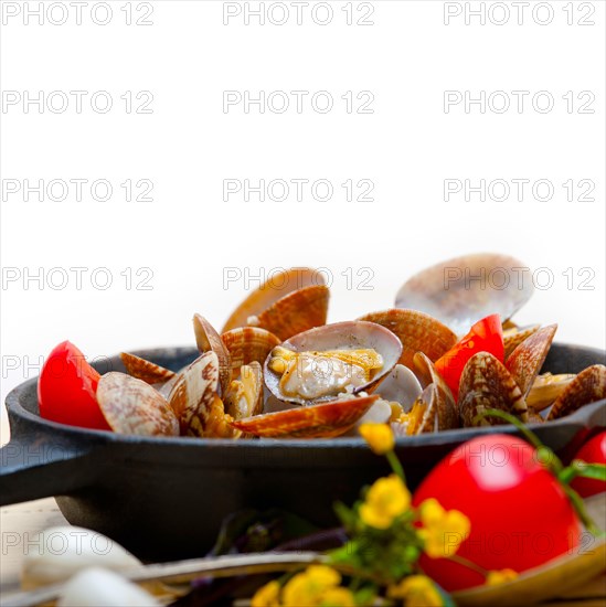 Fresh clams stewed on an iron skillet over wite rustic wood table