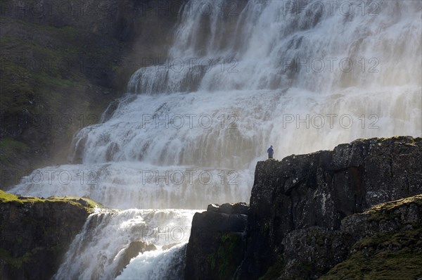 Man standing in front of falling masses of water from a waterfall