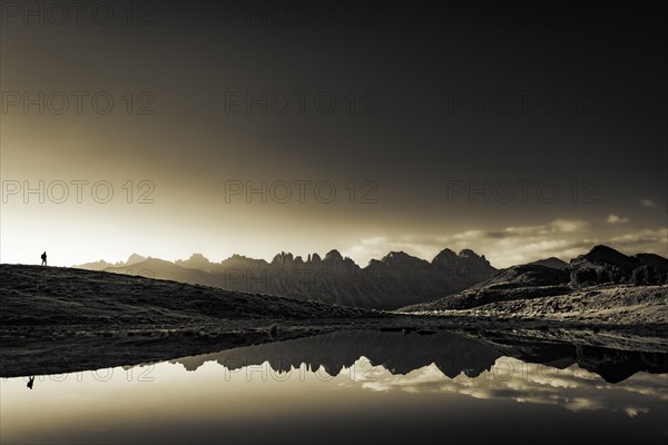 Salfainsee with reflection of the Kalkkoegel and mountaineers on mountain meadow at sunrise