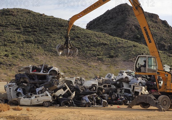 Crane piles scrap car on top of other cars