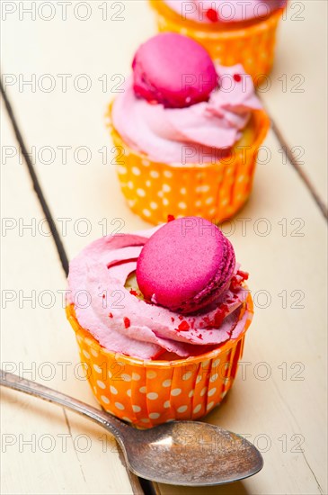 Fresh pink berry cream cupcake with macaroon on top over rustic wood table