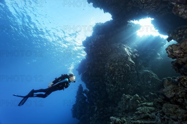 Divers in front of coral reef wall with breakthrough