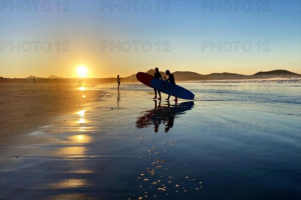 Surfers on Caleta de Famara beach at sunset