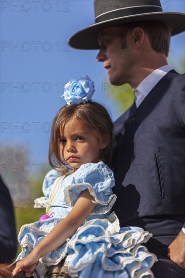 Portraits of a man and his daughter riding a horse in traditional attire during the Feria di Abril