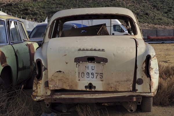 Rear view of beige scrapped Peugeot with painted number plate