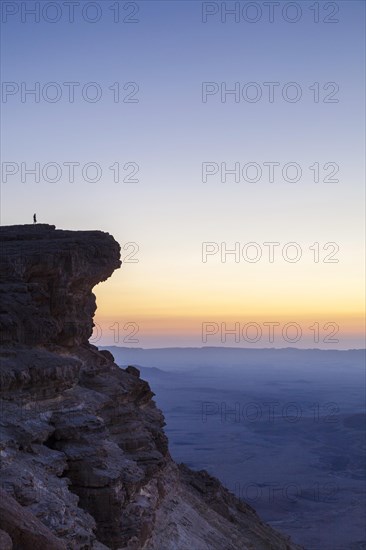 Alone figure on top of the cliffs overlooking the majestic desert of Makhtesh Ramon