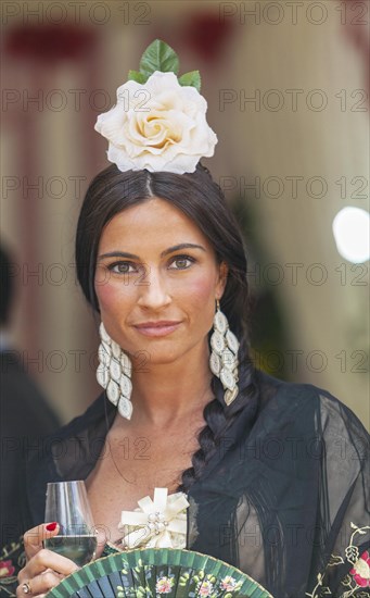 Portrait of a beautiful young woman in traditional attire and sherry glass in hand during the week-long Feria de Abril in Seville