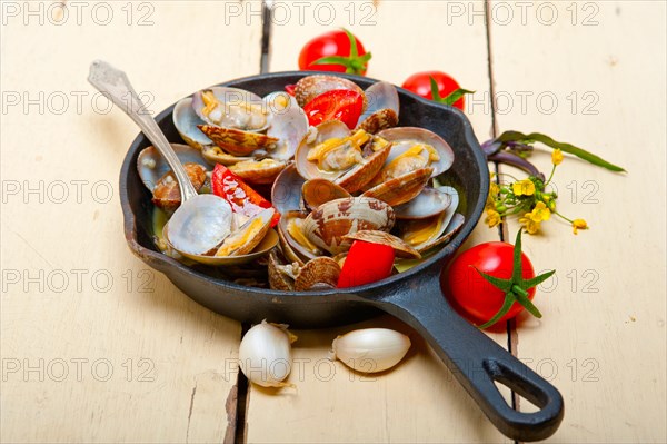 Fresh clams stewed on an iron skillet over wite rustic wood table