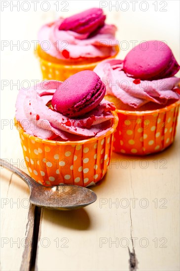 Fresh pink berry cream cupcake with macaroon on top over rustic wood table