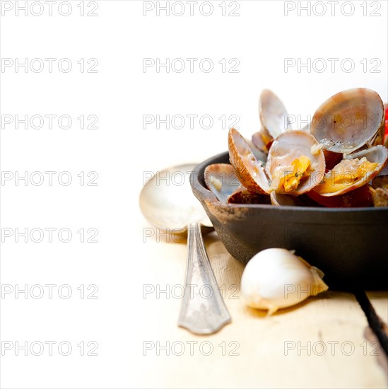 Fresh clams stewed on an iron skillet over wite rustic wood table