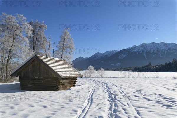 Winter landscape with snowshoe trails and haystack near frozen lake Barmsee
