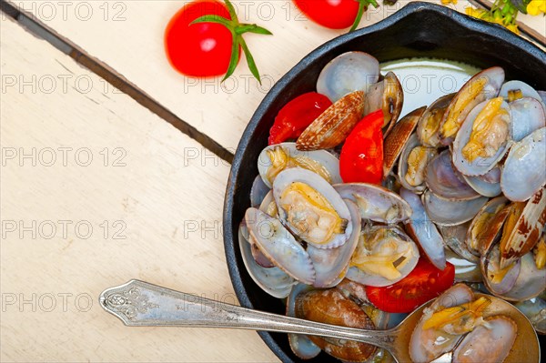 Fresh clams stewed on an iron skillet over wite rustic wood table