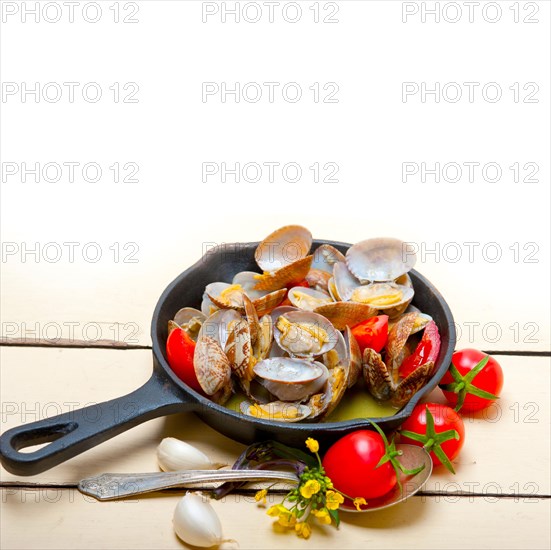 Fresh clams stewed on an iron skillet over wite rustic wood table