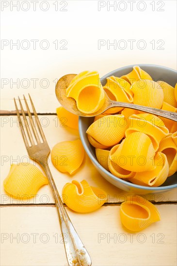 Raw Italian snail lumaconi pasta on a blue bowl over rustic table macro