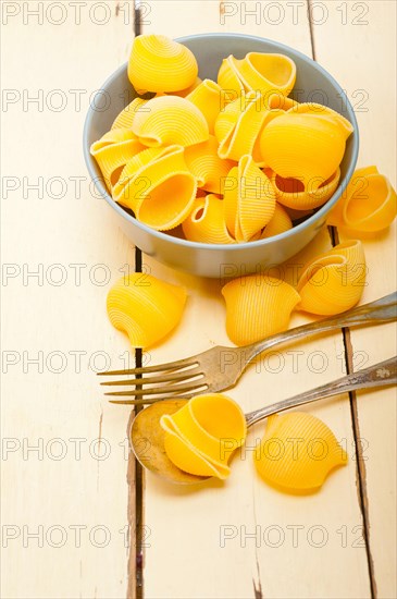 Raw Italian snail lumaconi pasta on a blue bowl over rustic table macro