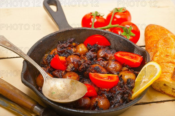 Baby cuttle fish roasted on iron skillet with tomatoes and onions over rustic wood table