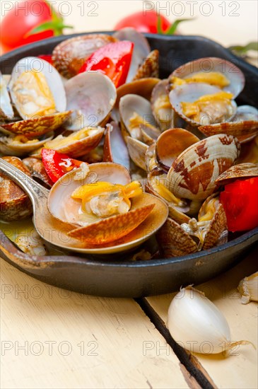 Fresh clams stewed on an iron skillet over wite rustic wood table