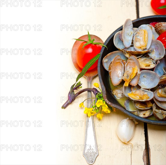 Fresh clams stewed on an iron skillet over wite rustic wood table