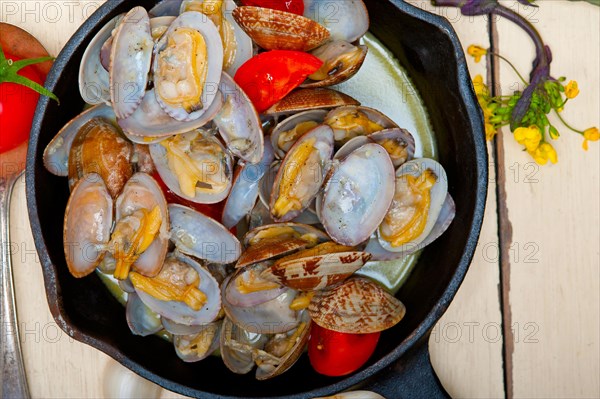 Fresh clams stewed on an iron skillet over wite rustic wood table