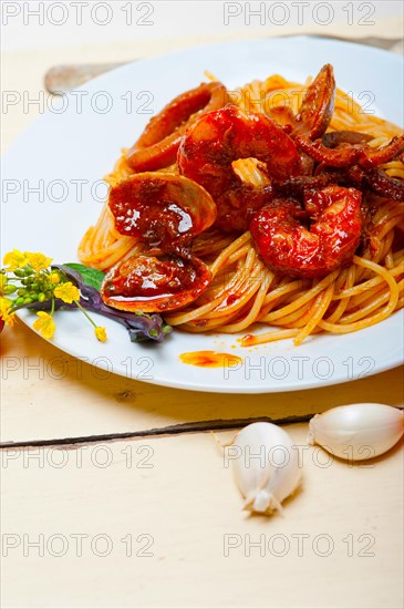 Italian seafood spaghetti pasta on red tomato sauce over white rustic wood table