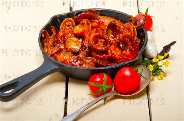 Fresh seafood stew prepared on an iron skillet ove white rustic wood table