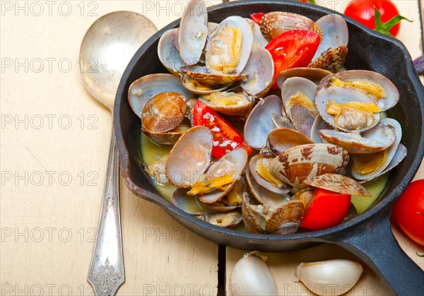 Fresh clams stewed on an iron skillet over wite rustic wood table