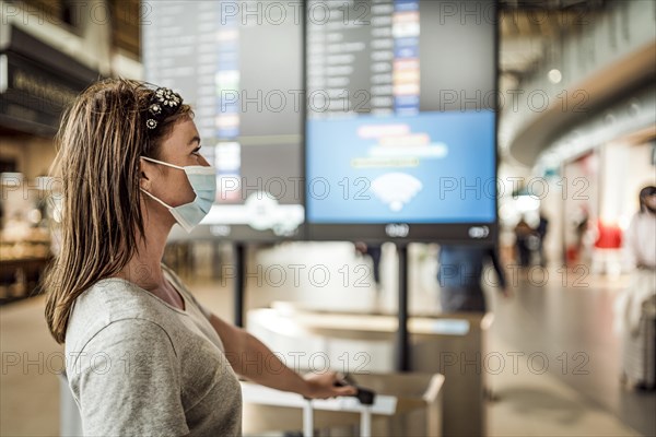 A young girl in mask waiting at the airport with flight information board as the background