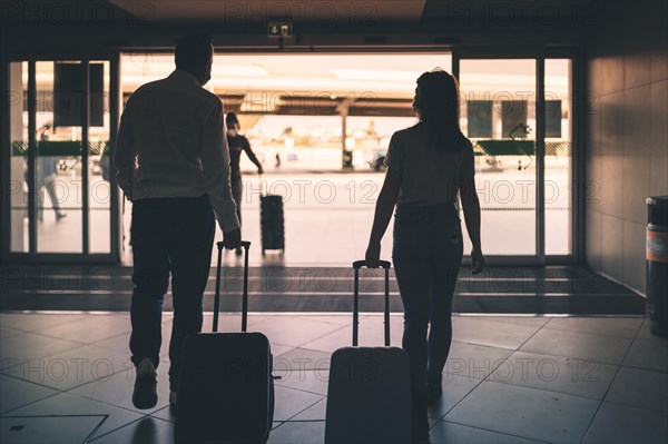 A couple of friends with luggage wearing protective masks leaving the airport