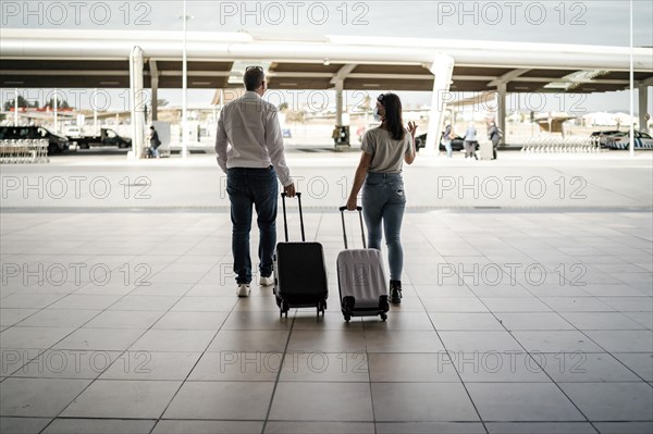 A couple of friends with luggage wearing protective masks leaving the airport