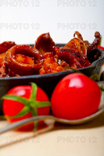 Fresh seafood stew prepared on an iron skillet ove white rustic wood table