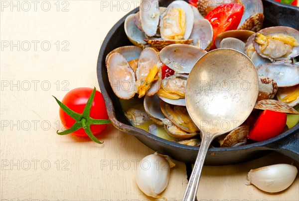 Fresh clams stewed on an iron skillet over wite rustic wood table