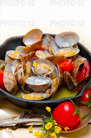Fresh clams stewed on an iron skillet over wite rustic wood table
