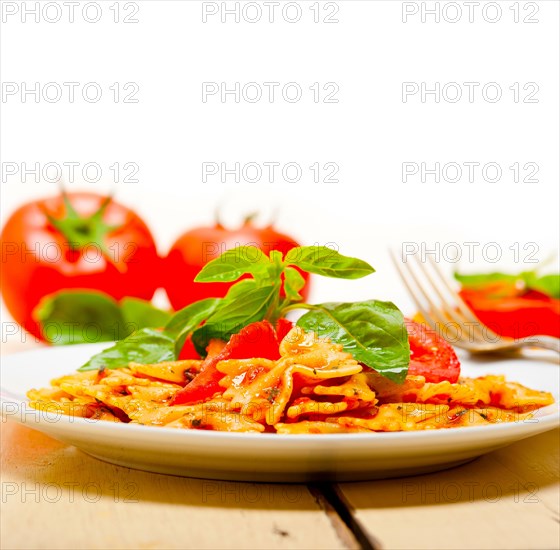 Italian pasta farfalle butterfly bow-tie with tomato basil sauce over white rustic wood table