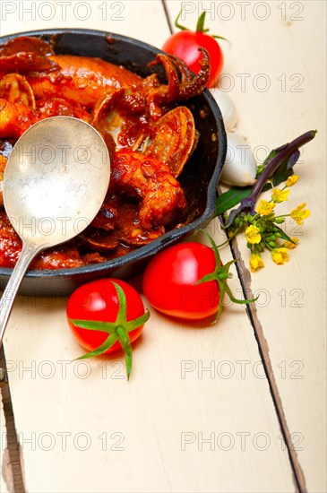 Fresh seafood stew prepared on an iron skillet ove white rustic wood table