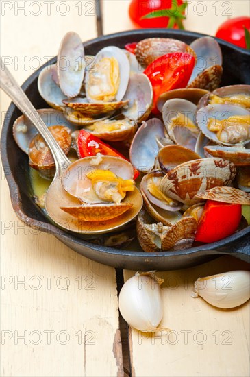 Fresh clams stewed on an iron skillet over wite rustic wood table