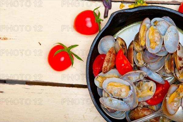 Fresh clams stewed on an iron skillet over wite rustic wood table