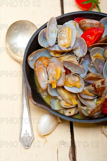 Fresh clams stewed on an iron skillet over wite rustic wood table