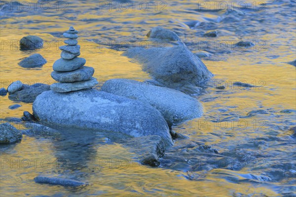 Stack of stones on mountain stream with reflecting larches in the water