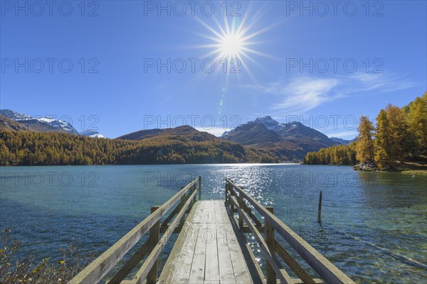 Wooden jetty on lake with sun in autumn